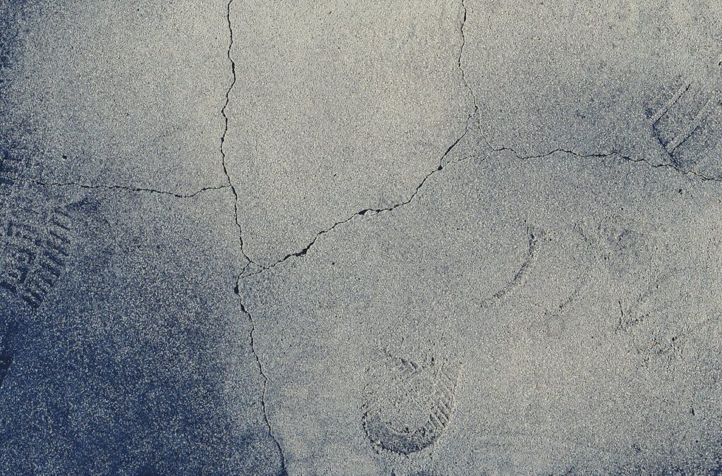 Detailed close-up of cracked pavement texture with visible footprints for texture design use.